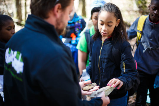 Muddy Sneakers instructor holds different rocks up for an Isenberg Elementary student to examine