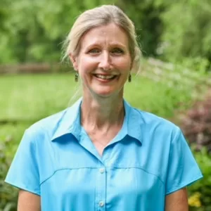 Headshot of Anne Bullard smiling at the camera in front of lush greenery.