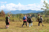 Students walk across grassy field in the foreground, with a forest backed by Blue Ridge mountains in the background.