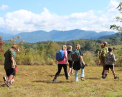 Students walk across grassy field in the foreground, with a forest backed by Blue Ridge mountains in the background.