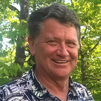 Headshot of Rick Houck smiling at the camera in front of lush greenery.