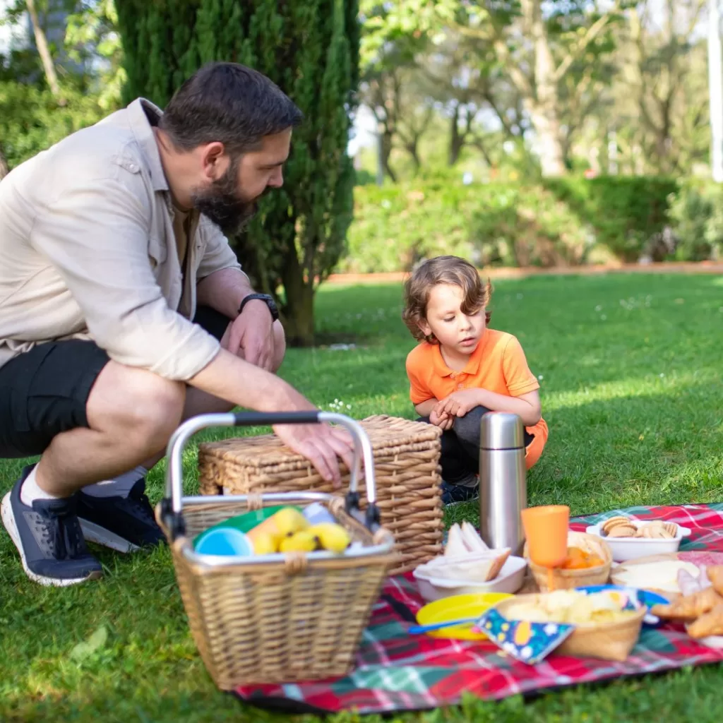 Father and son having a picnic on a grassy field in a park.