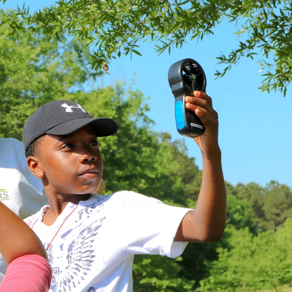 Student uses an anemometer to study wind speed during a weather field trip.