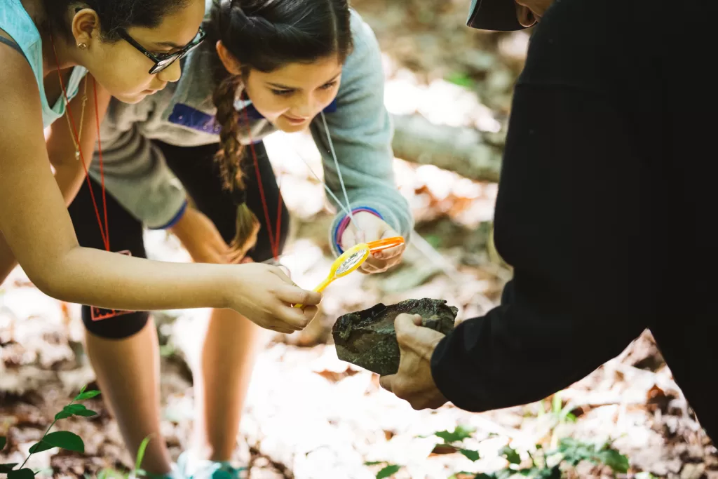 Students use magnifying glasses to examine organisms found on a rock.