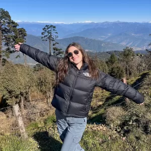 Aila Music, Muddy Sneakers Intern, posing for a photo atop a mountain, with mountains and sky meeting in the background