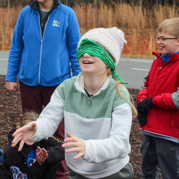 A smiling student, wearing a blindfold, with arms stretched out in front of them during a active game of Bat and Moth
