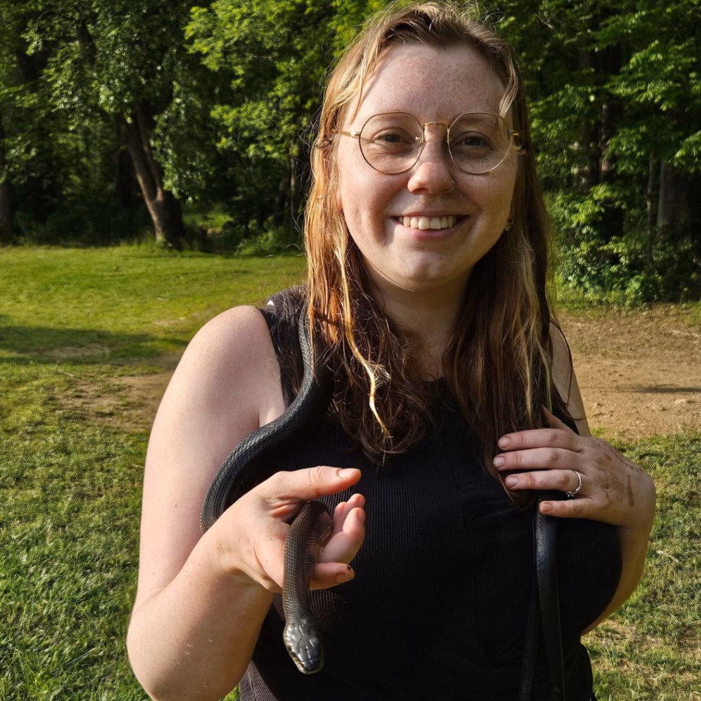 Eden Simmons smiling at the camera, posing with a black snake.