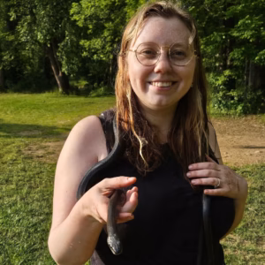 Eden Simmons smiling at the camera, posing with a black snake.