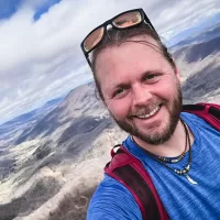 Cody "Finn" Finney standing atop a mountain smiling at the camera.