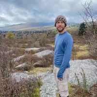 Robert Schmidt stands amid a rocky valley, with mountains shrouded in cloud in the distance.